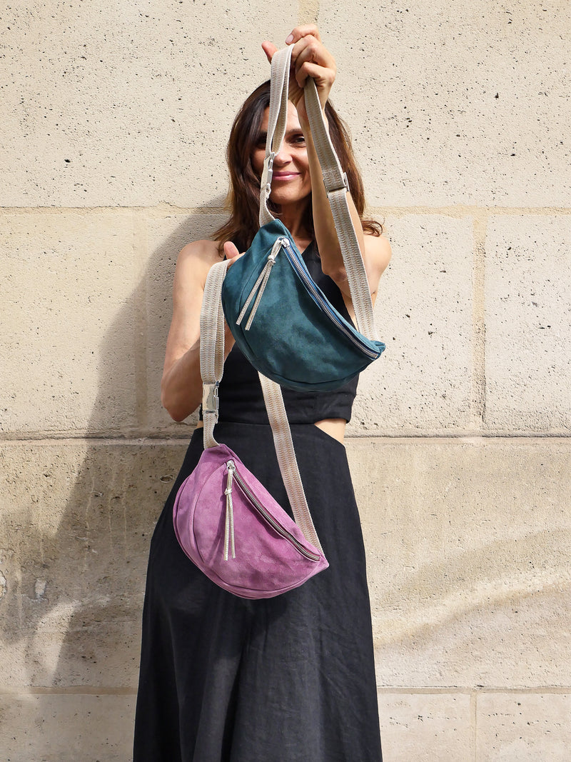 Petrol green and violet suede belt bag with gold leather zip puller worn on a black dress