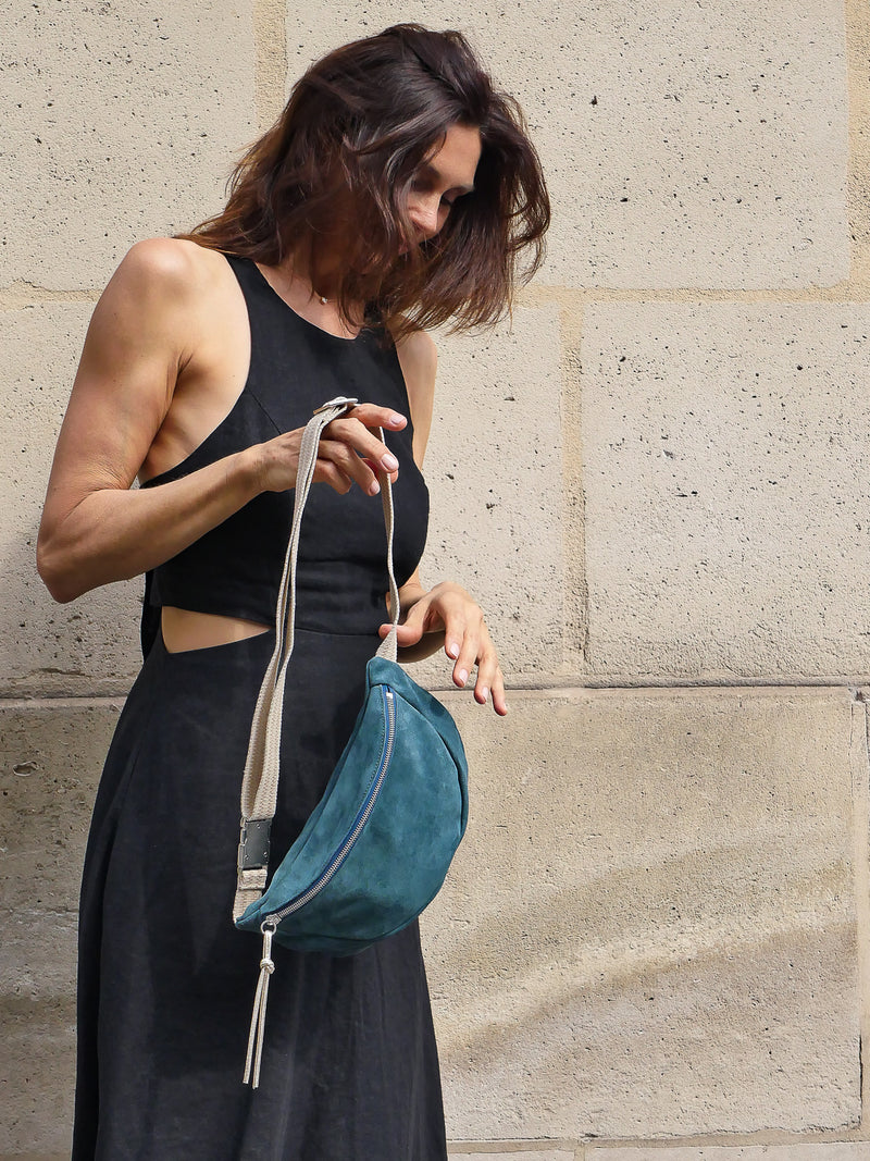 Petrol green suede belt bag with gold leather zip puller worn on a black dress