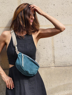 Petrol green suede belt bag with gold leather zip puller worn on a black dress