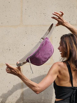 Violet suede belt bag with gold metallic leather zip puller held up by a beautiful woman