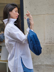 Satin nylon sling bag in sapphire blue with shiny silver hardware and long strap, worn by a girl in the streets of Paris.