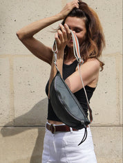Dark grey satin nylon fanny pack designed and made in Paris with a striped  adjustable crossbody strap, worn by a Parisian beauty on the streets of Paris.