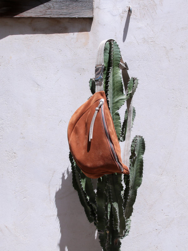tan suede belt bag with gold metallic leather zip puller hanging on a cactus
